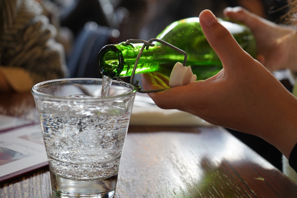 a hand holding a green object above a glass of water