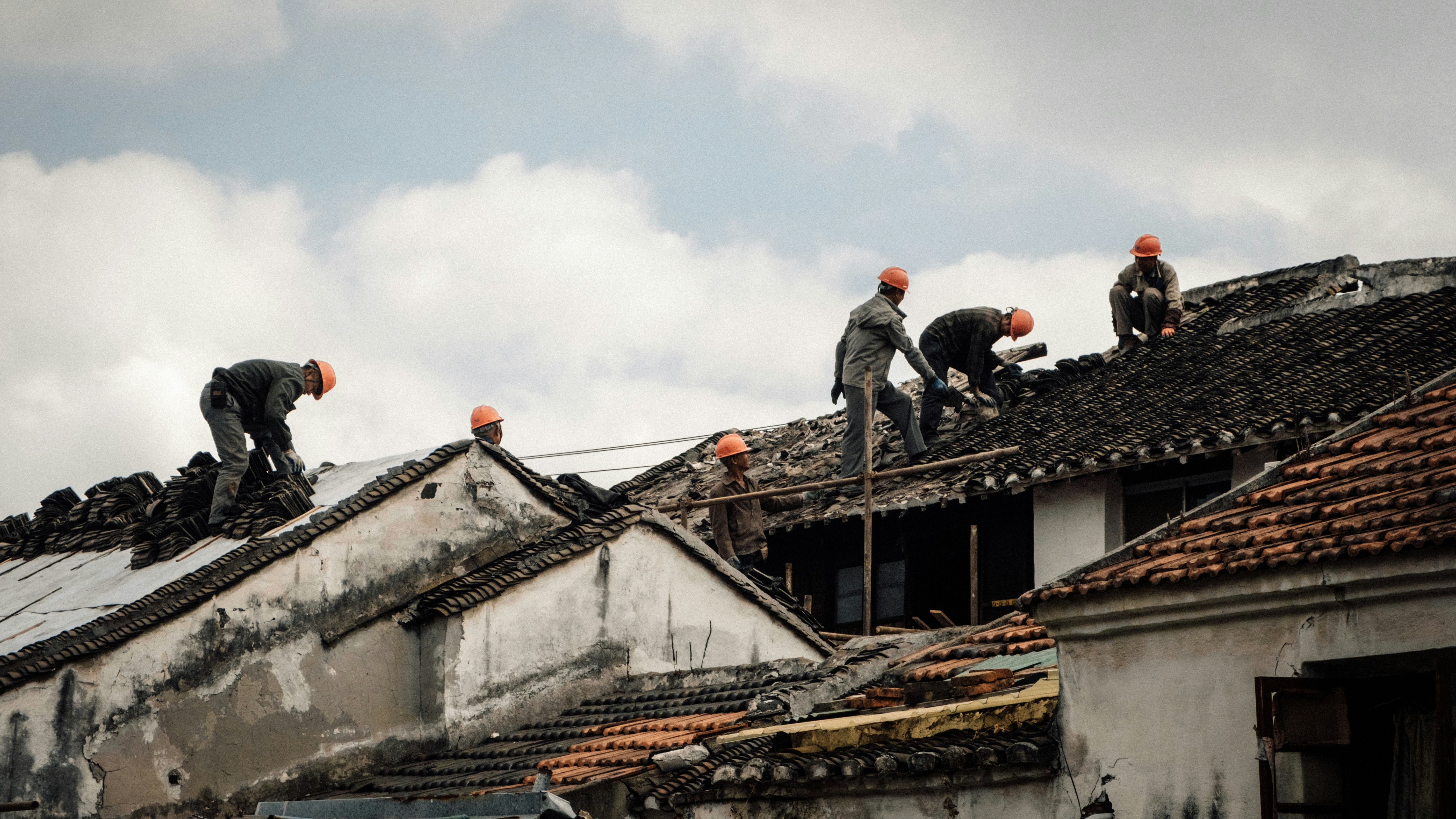 roofers wearing safety harnesses working on a steep residential roof pitch - roof replacement cost guide for homeowners