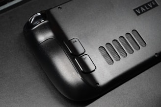 The image features a close-up view of a black gaming controller with visible buttons labeled R4 and R5. The surface appears sleek and matte, with a grid-like vent design next to the buttons. A partial brand name, 'VALVE', is visible in the corner.