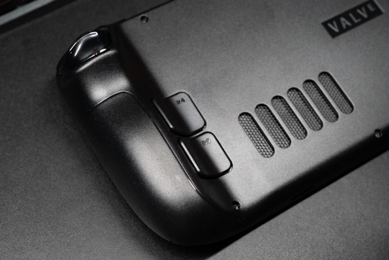The image features a close-up view of a black gaming controller with visible buttons labeled R4 and R5. The surface appears sleek and matte, with a grid-like vent design next to the buttons. A partial brand name, 'VALVE', is visible in the corner.
