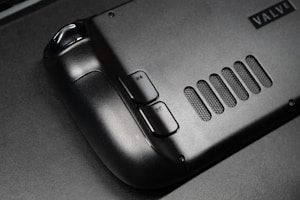 The image features a close-up view of a black gaming controller with visible buttons labeled R4 and R5. The surface appears sleek and matte, with a grid-like vent design next to the buttons. A partial brand name, 'VALVE', is visible in the corner.