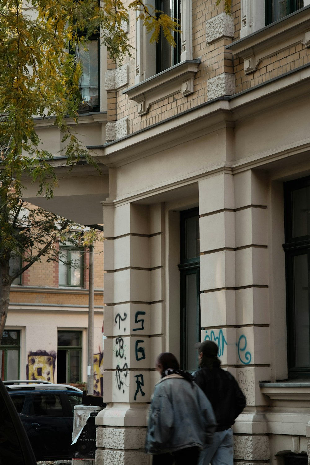 a couple of people walking down a sidewalk next to a building