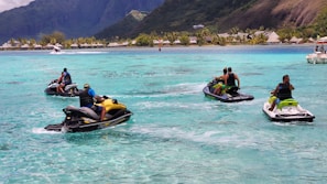 A group of friends laughing on jet skis cutting through sparkling blue water under a sunny sky
