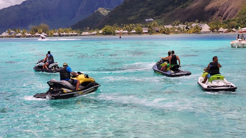 A group of friends laughing and riding jet skis on sparkling blue water under a sunny sky.
