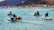 Four people riding jet skis on clear turquoise water with lush green mountains and bungalows in the background.