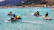 Friends laughing together while riding waterbikes near a tropical coastline.