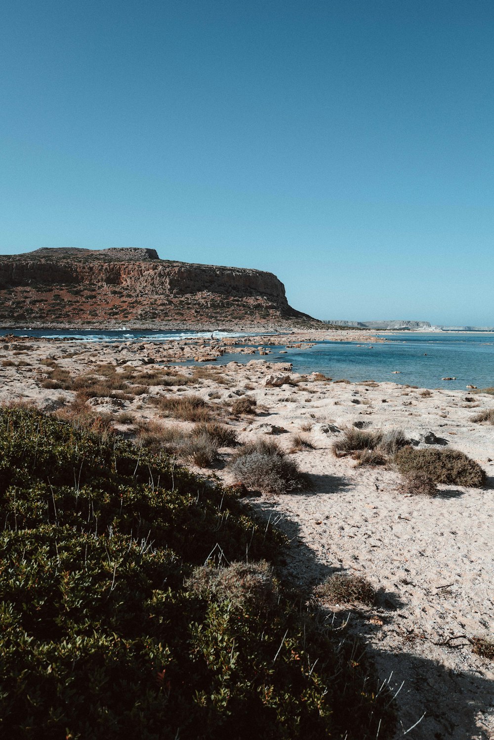 a sandy beach with a hill and water in the background