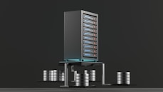 A digital rendering depicting a tall, metallic server rack positioned centrally on a platform. The server appears to have multiple blue-lit slots. Surrounding the rack, there are several stacks of cylindrical objects resembling databases or storage units, all set against a dark background.