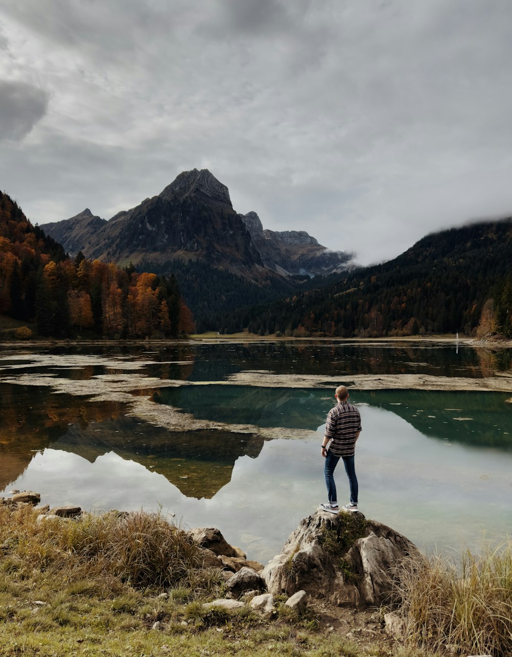 um homem de pé em uma rocha perto de um lago com montanhas ao fundo