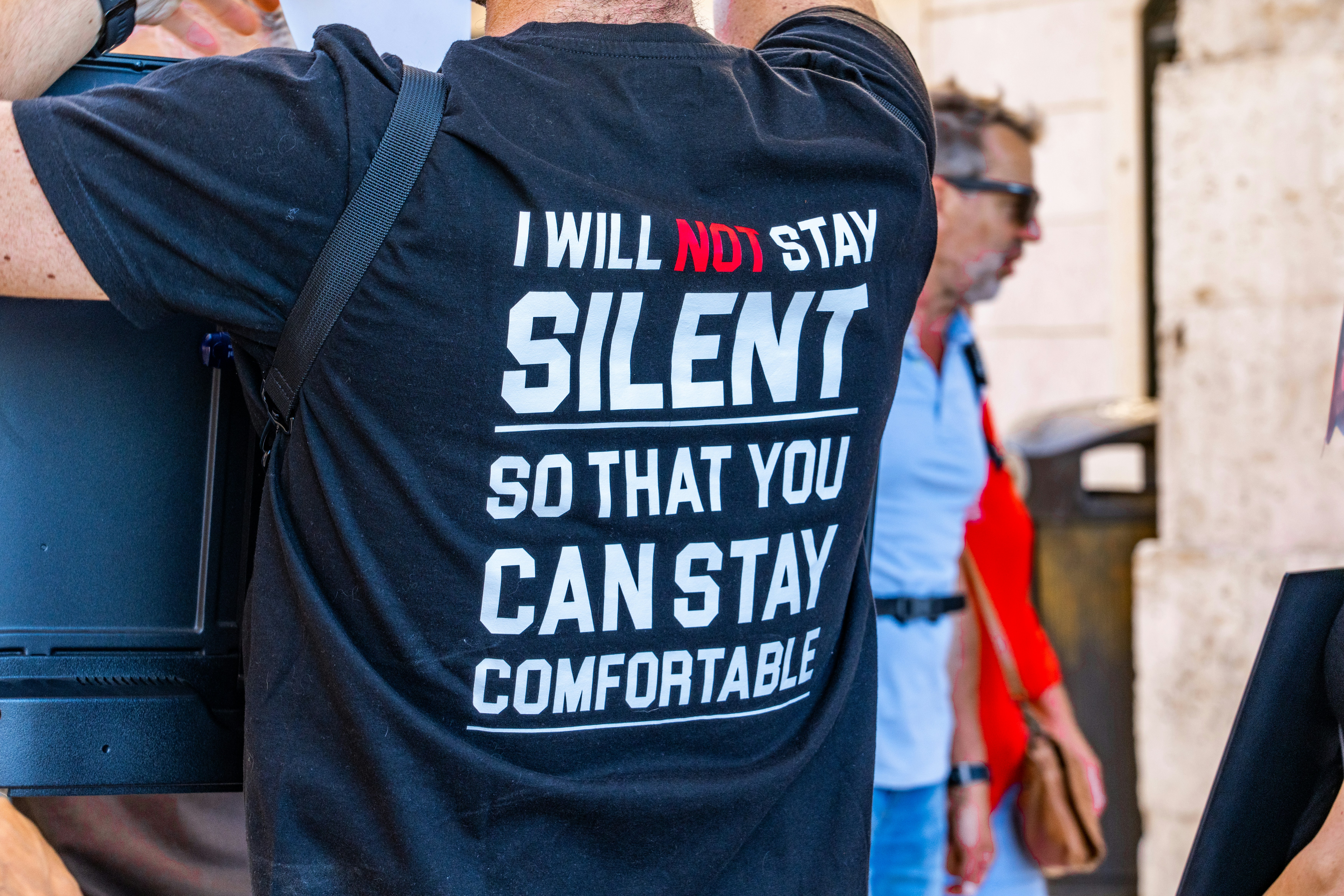 a person wearing a backpack, political t-shirt saying "I will not stay silent so that you can stay comfortable"