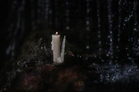 Close-up of a handmade cauldron candle flickering gently on a moss-covered stone.