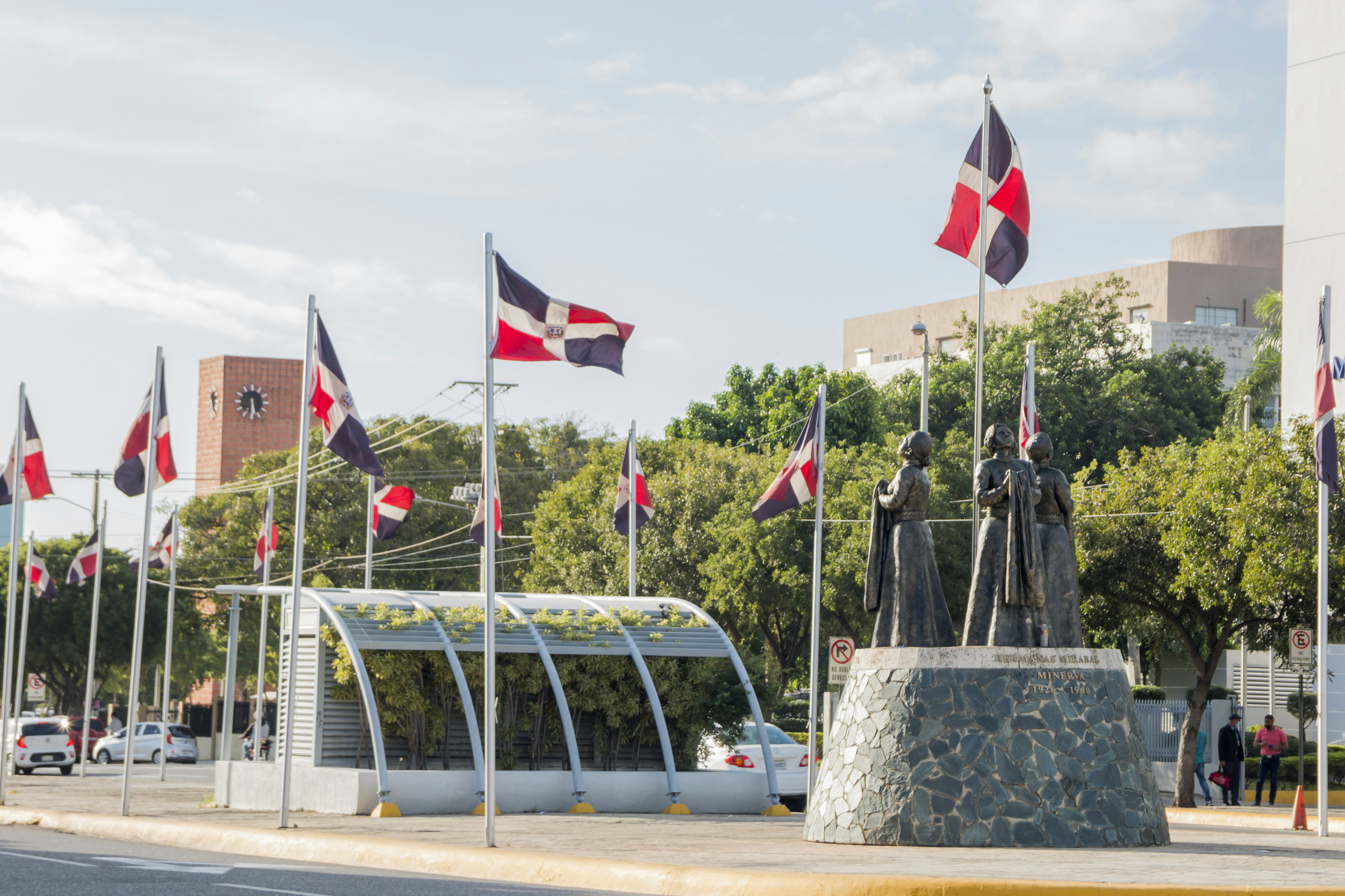 Une place publique animée avec une fontaine centrale, des statues et des drapeaux nationaux.