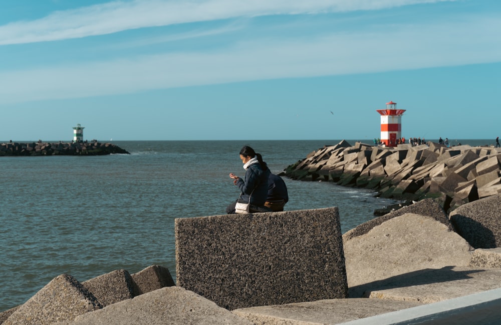 a man sitting on a stone wall by a lighthouse