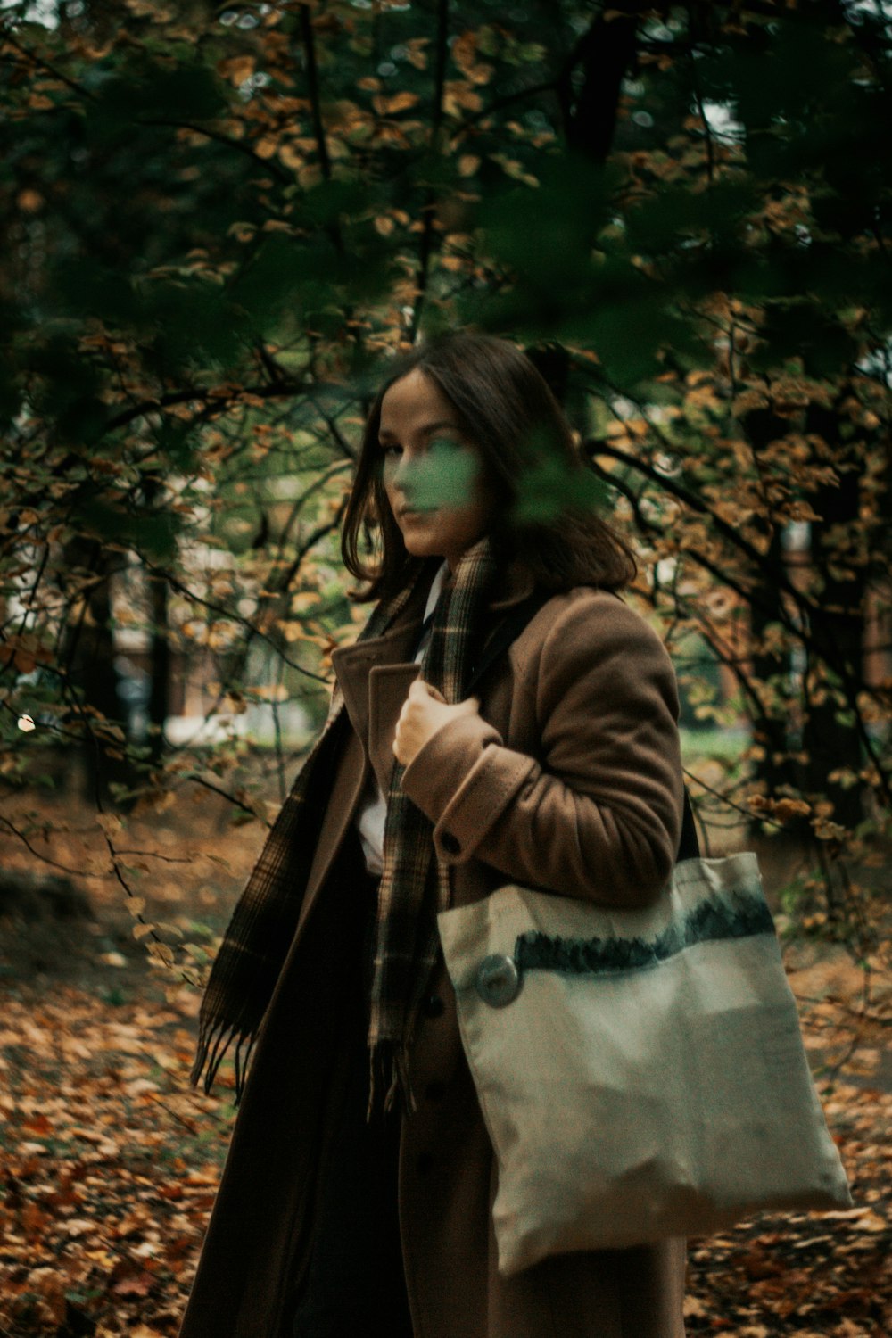 a woman with a scarf around her head and a coat in a forest