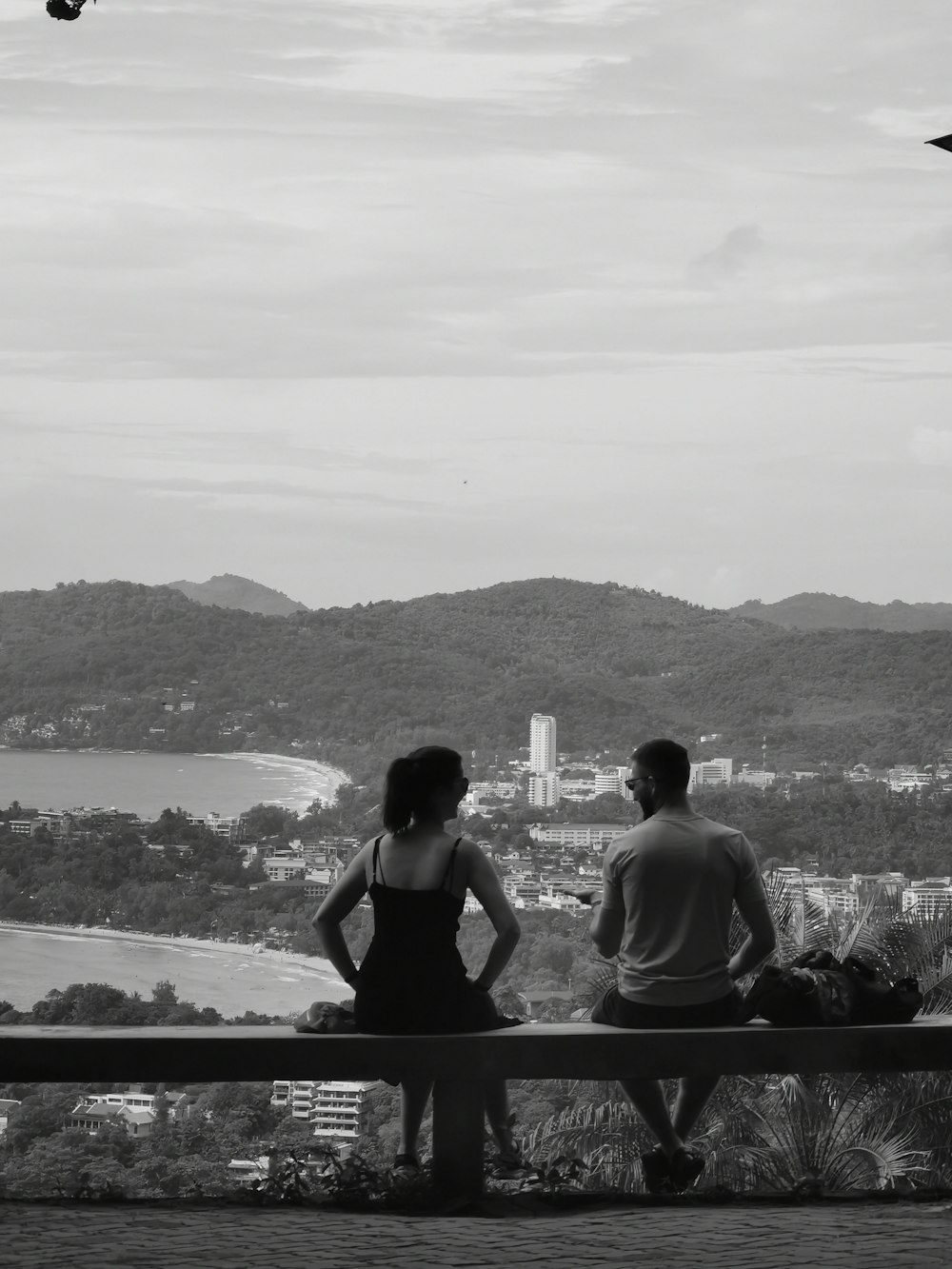 a man and woman sitting on a bench looking at the water