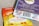 A close-up view of two packages of edible gummies on a textured surface. One package has a blue and purple design with information about 'Live Rosin Gummies,' including a 250mg THC content and '100% hemp derived' labeling. The other package is orange and yellow, labeled as 'Legal Cannabis Space Gummies' with 300mg THC content. Both packages have QR codes, branding, and legal information.