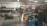 A person is using a grinding tool, creating bright sparks in an industrial workshop. The space contains various metal pipes, pallets, a blue welding machine, and shelves stocked with containers.