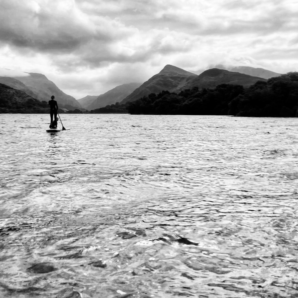 Una persona en una tabla de paddle en un lago con montañas al fondo