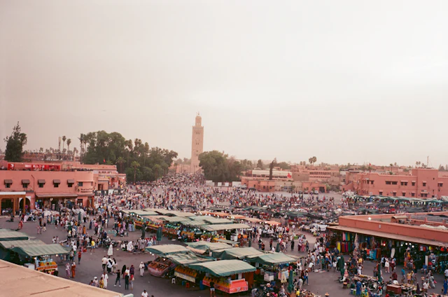 Elevated view over the crowded Jemaa el-Fnaa square and market stalls with the Koutoubia minaret in the distance.