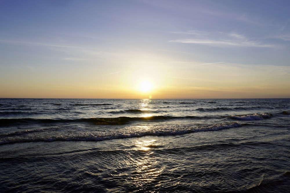 a beach with waves and the sun setting