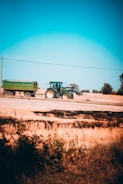 A tractor pulling a trailer loaded with farming supplies on a sunny day.
