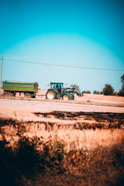 A tractor loaded with produce crossing a weighbridge surrounded by green fields under a clear sky.