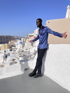 A traveler happily taking a selfie at a scenic overlook with white buildings and blue domes in the background.