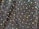 A textured fabric with an intricate pattern of small, shiny beads and larger iridescent sequins. The sequins reflect a spectrum of colors, creating a vibrant, shimmering effect against the dark background.