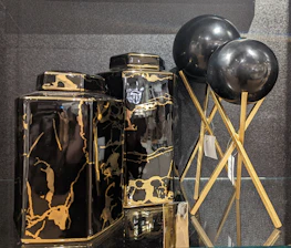 Two black and gold marble-patterned vases are displayed alongside two black spherical objects on golden stands. The vases have a glossy finish, with the marble pattern adding a luxurious touch. The spherical objects appear to be decorative, supported by elegant crisscrossed stands.