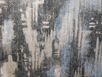 An abstract painting with textured brush strokes creates a sense of depth. The artwork features a mix of dark and light areas, blending shades of gray, blue, and cream. The blurred effect gives a mysterious and enigmatic vibe.