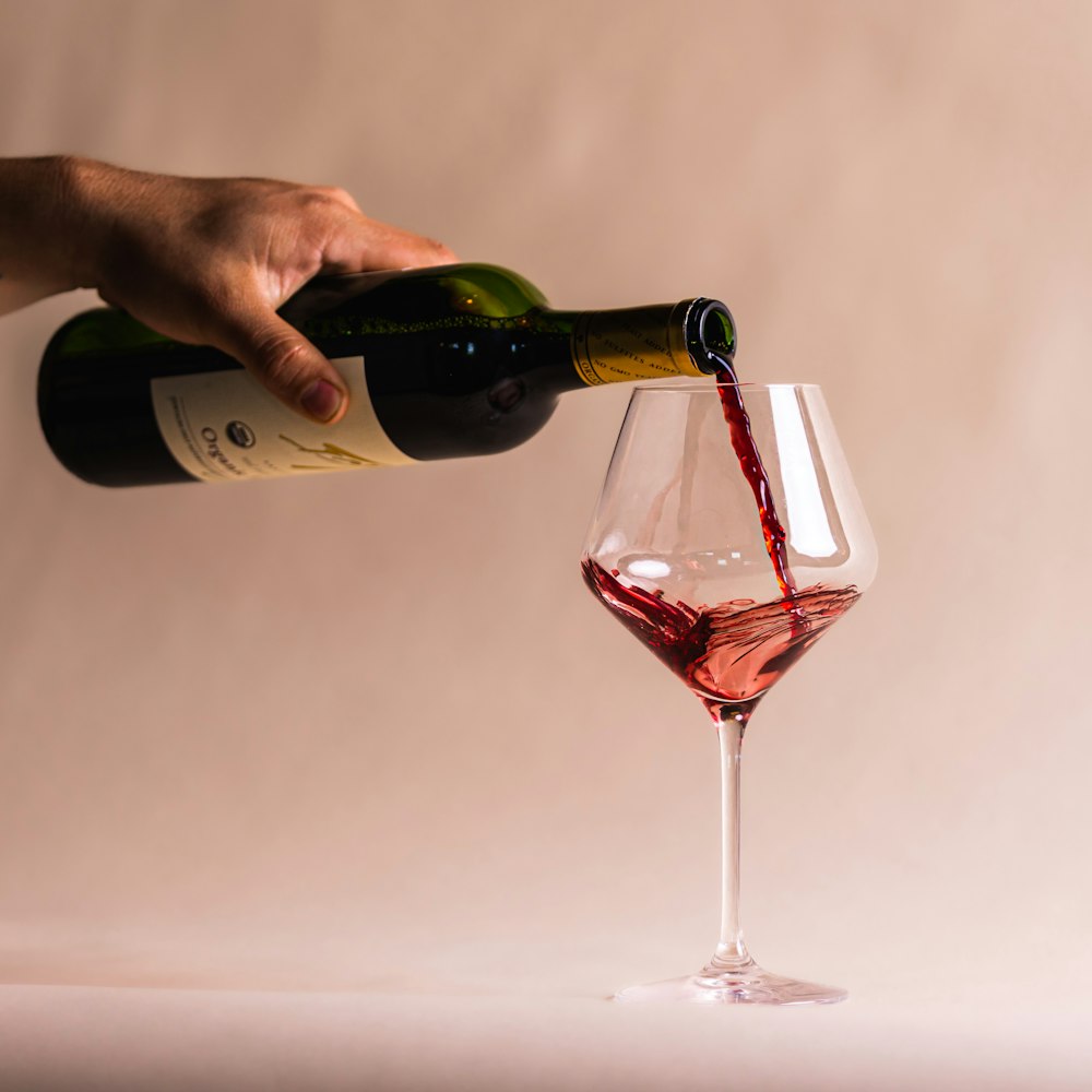 a hand pouring a glass of red wine into a glass