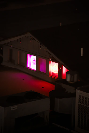 A shadowy rooftop party glowing with deep red neon lights against a night cityscape.