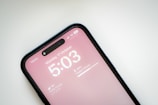 A smartphone screen displays a time of 5:03 PM on Monday, 17 October. The device is connected to a mobile network with 5G and displays a battery percentage of 60%. The background is a soft pink, and the weather information shows partly cloudy with a temperature of 16°C. The phone is recognized as an iPhone, situated against a plain background.