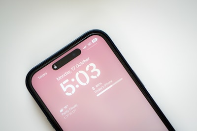 A smartphone screen displays a time of 5:03 PM on Monday, 17 October. The device is connected to a mobile network with 5G and displays a battery percentage of 60%. The background is a soft pink, and the weather information shows partly cloudy with a temperature of 16°C. The phone is recognized as an iPhone, situated against a plain background.
