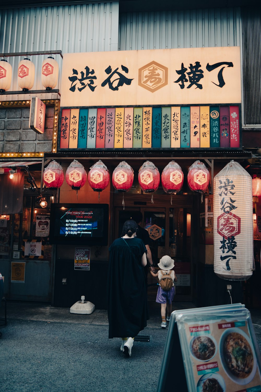 a person and a child walking in front of a store with lanterns