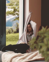 Relaxed woman wearing comfy trousers and a light jacket, sitting by a cozy window.