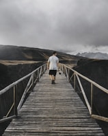 An adventurer crossing a wooden bridge with mountains in the background, guided by a digital travel app.