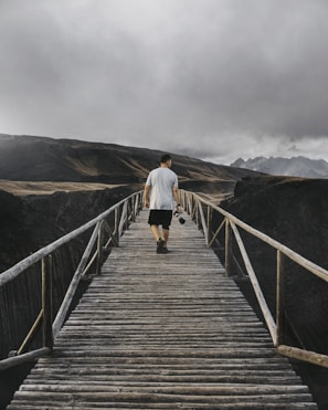 An adventurer crossing a wooden bridge with mountains in the background, guided by a digital travel app.