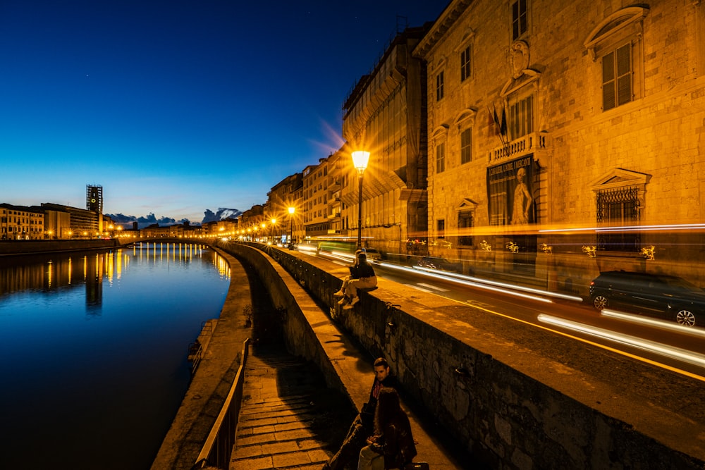 a person sitting on a bench next to a river at night