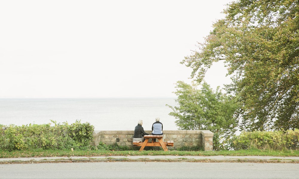 a couple of people sitting on a bench by the water