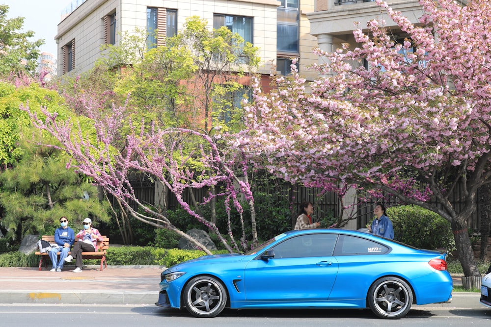 a blue car parked on the side of a road with pink trees