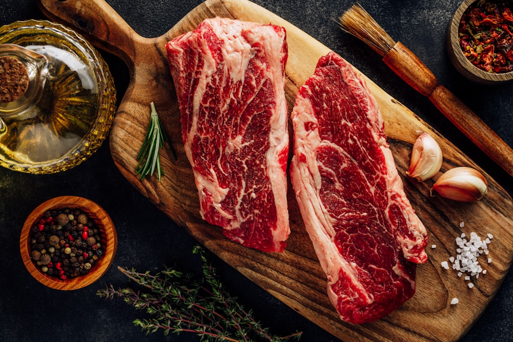 a slab of raw meat on a cutting board with vegetables and a bowl of sauce