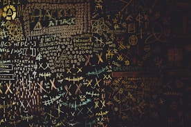 A chaotic chalkboard filled with various symbols, numbers, and text related to hacking. Words like 'HACKER', 'ATTACK', and 'UPLOAD' are prominently visible amidst a jumble of codes and cryptic symbols. The board conveys an atmosphere of mystery and complexity, reminiscent of a hacker's workspace.