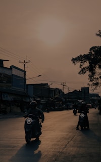 Riders cruising along a coastal road, the sun setting behind them casting long shadows.