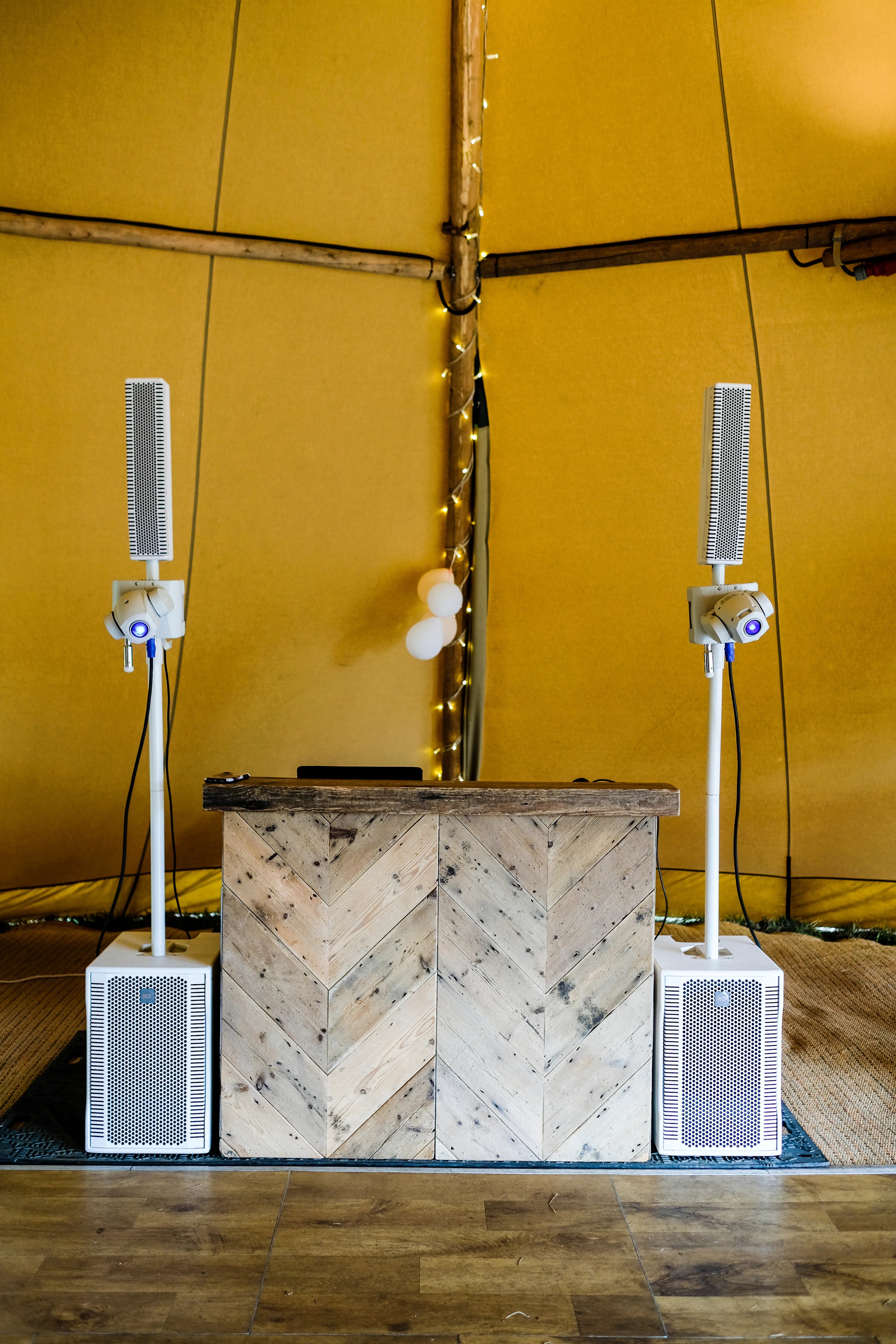 A DJ booth with a wooden facade set up inside a wedding tent