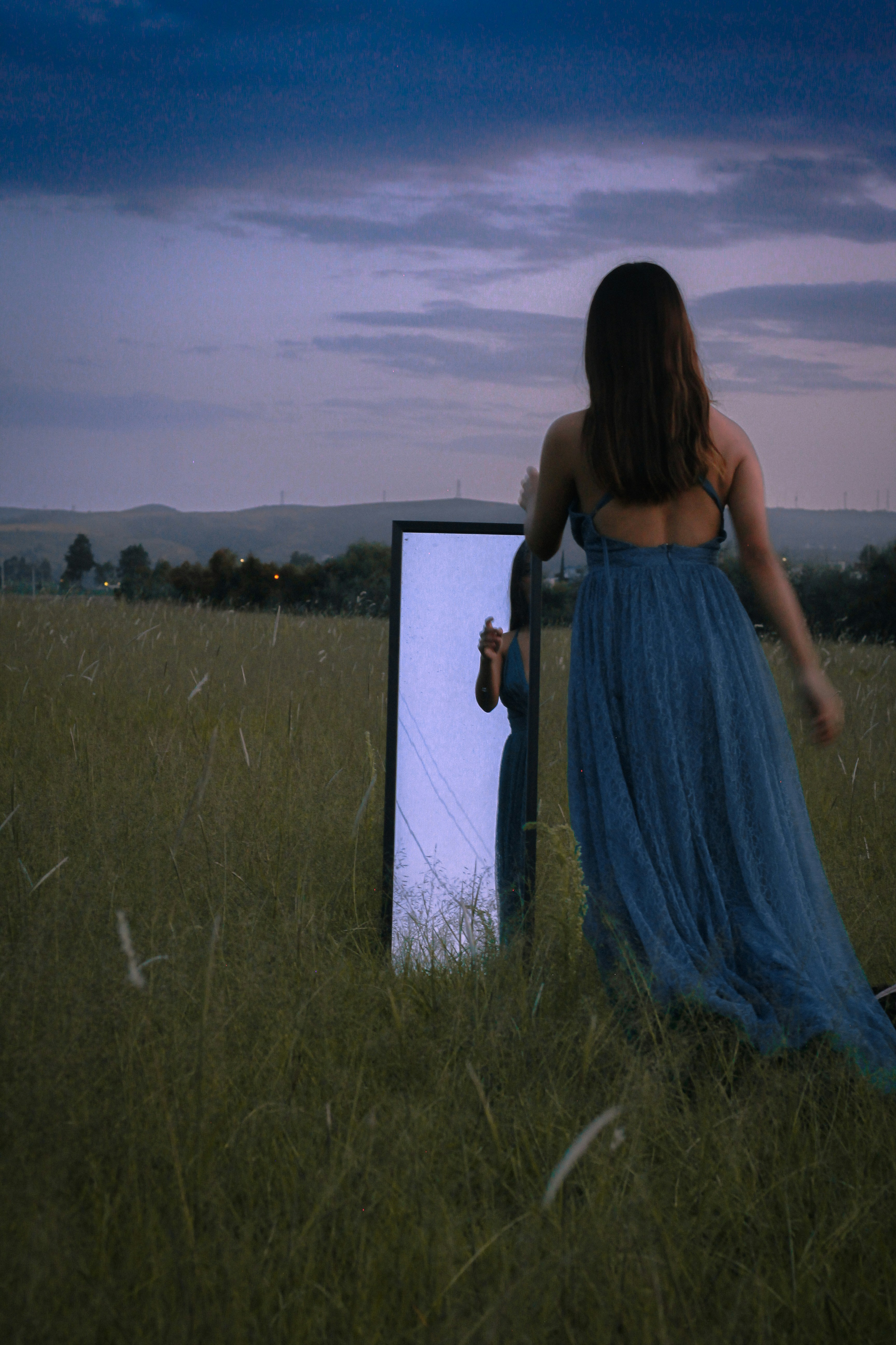 A person in a dress standing in a field with a blue wall and a blue sky ...