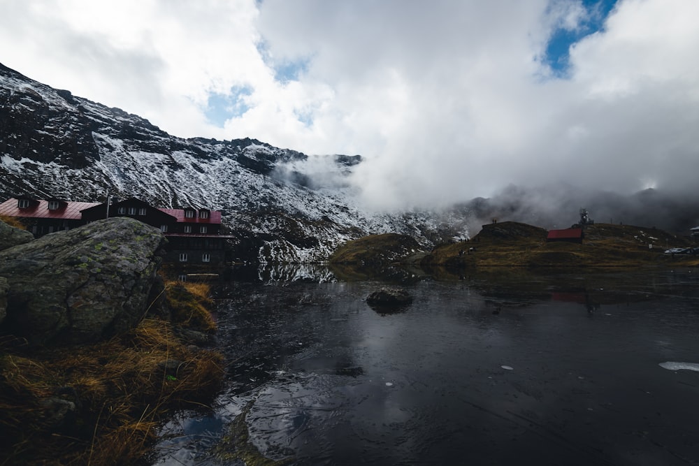 a building on a cliff by a lake with mountains in the background