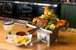 A rustic wooden table set with grilled meats and bowls of chimi gel ready to be shared