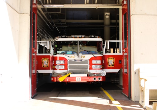 A fire truck is parked inside a garage with its doors open, revealing the shiny red exterior and various firefighting equipment attached to the front.
