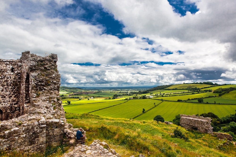 a person sitting on a rock ledge overlooking a green valley